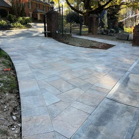 Newly installed patterned stone driveway leading to a brick house with black iron gates and autumn trees.