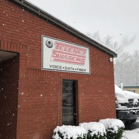Snow falling outside a brick building with Telenet Systems sign offering voice, data, and fiber services.