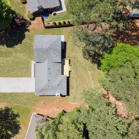 Aerial view of a single-story house with a driveway and surrounding green trees on a sunny day