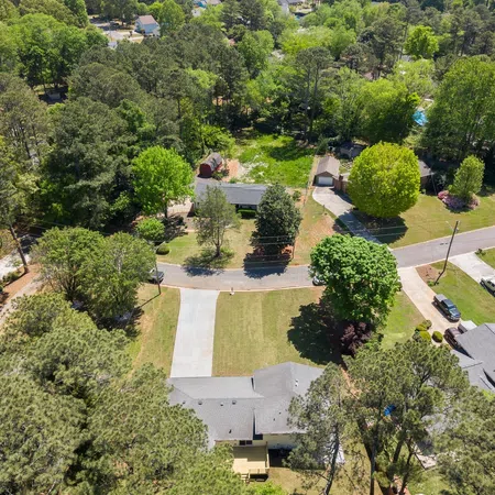 Aerial view of suburban neighborhood with houses, trees, lawns, and a circular street on a sunny day.