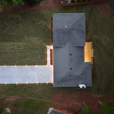 Aerial view of a suburban house with newly lit driveway and landscaped yard at dusk