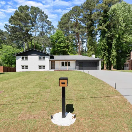 Modern split-level house with a large lawn, black mailbox on a post, and a wide concrete driveway under blue sky.