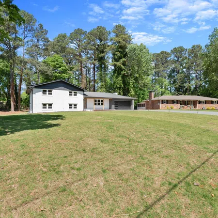 Two suburban houses with spacious green lawns and tall trees under a clear blue sky on a sunny day