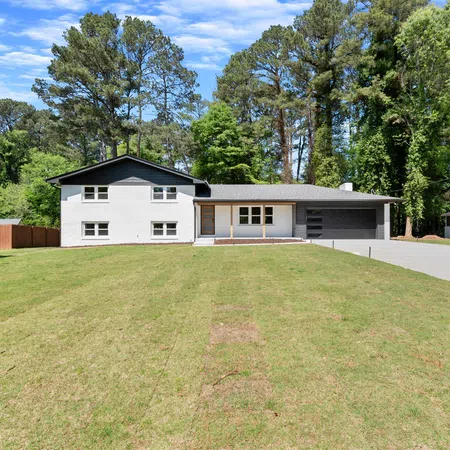 Modern split-level white house with large lawn and tall trees under a partly cloudy blue sky