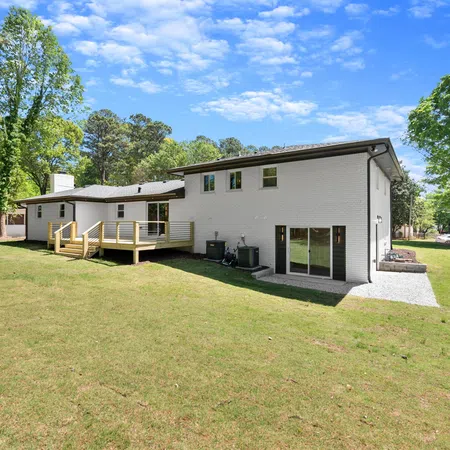 Modern white brick two-story house with a spacious backyard and wooden deck under a sunny blue sky.