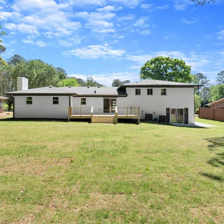 Spacious backyard with green lawn and white two-story house under blue sky with trees surrounding it