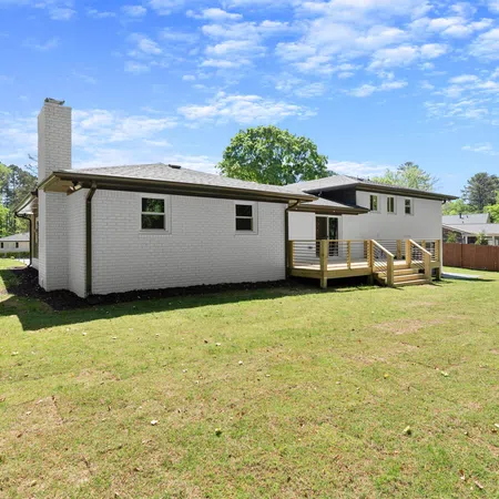 Modern white brick house with large backyard and wooden deck under a clear blue sky on a sunny day