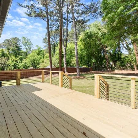 Spacious wooden outdoor deck with metal railing overlooks a green yard with tall trees under a clear sky