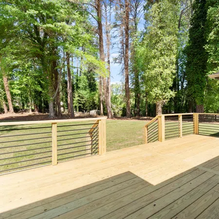 Spacious wooden deck overlooking a green backyard with tall trees under a clear blue sky.