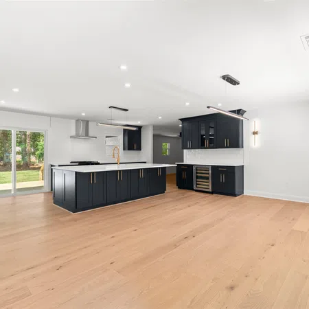 Spacious modern kitchen with black cabinetry, wood floors, white walls, and large sliding glass doors opening to yard.