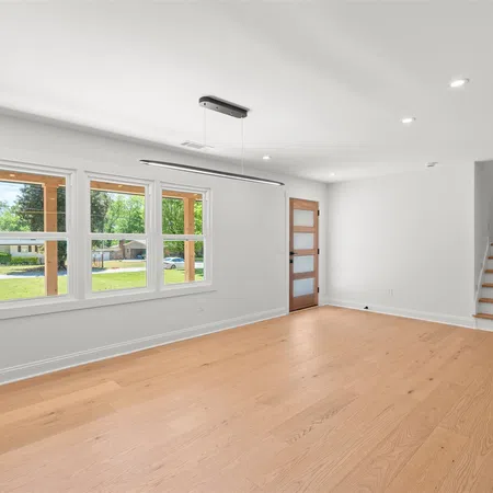 Bright empty room with large windows, wooden floor, white walls, modern ceiling light, and staircase.