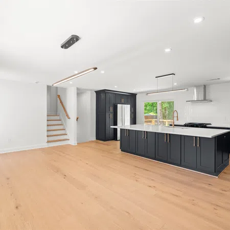 Bright modern kitchen with black cabinets, white countertops, hardwood floors, and large center island with pendant lights.