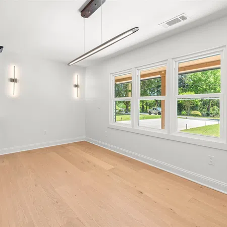 Bright modern room with light wood flooring, black cabinets, white walls, and large windows with outdoor view