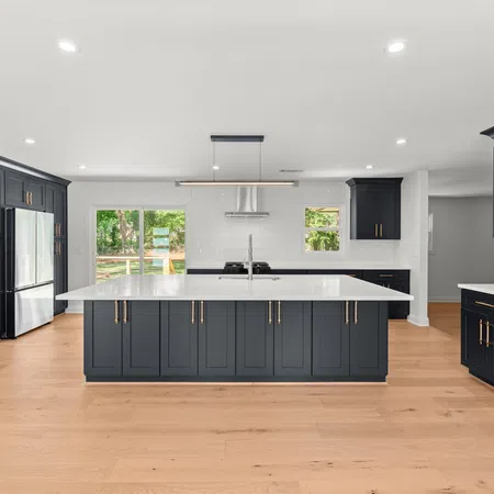 Modern kitchen with dark gray cabinets, large white island, stainless appliances, and wood flooring under natural light