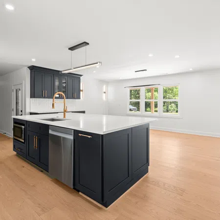 Modern kitchen with navy blue island, white countertops, hardwood floors, and stainless steel appliances in open floor plan.
