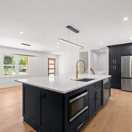 Modern kitchen with black cabinetry, white countertops, large island, gold fixtures, stainless steel appliances, and wood flooring.