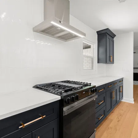Modern kitchen with navy cabinets, white countertops, stainless steel stove, hardwood floors, and a white backsplash.