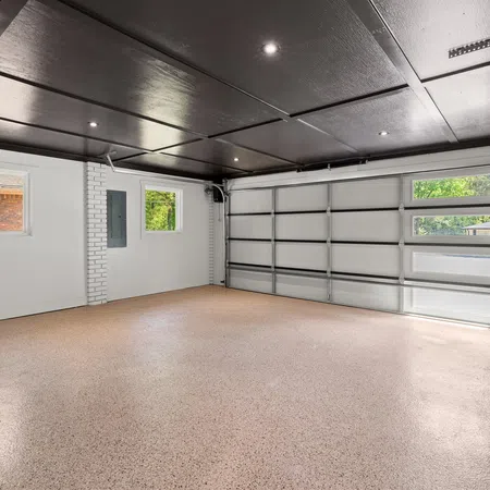 Empty clean garage with polished floor, white brick walls, windows, and a closed sectional garage door.