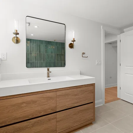 Modern bathroom with wood vanity, white countertop, rectangular mirror, and brass sconces in bright natural light