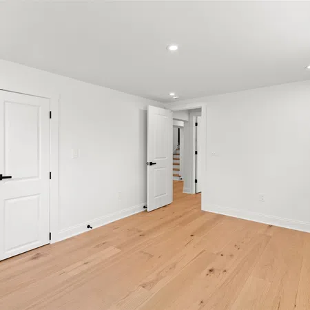 Empty white room with light wood flooring, white doors, and recessed ceiling lights in a modern home.