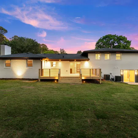 Modern two-story brick house with illuminated deck and spacious green lawn at sunset under a vibrant sky