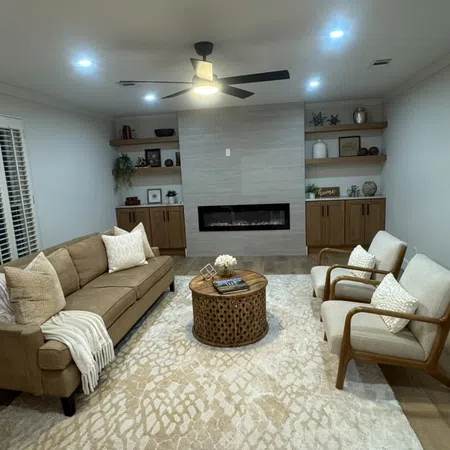 Modern living room with beige sofa, two armchairs, round wooden coffee table, patterned rug, and built-in fireplace.