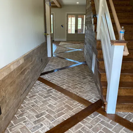 Entryway with unique brick-patterned flooring intersected by diagonal wooden strips and wooden staircase on the right.