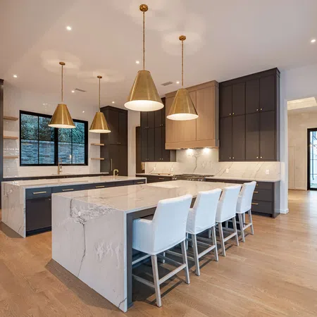 Modern kitchen with marble island, gold pendant lights, dark cabinetry, and white bar stools on wood floors