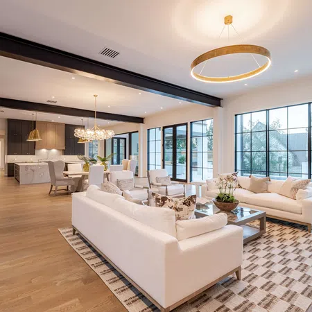 Spacious modern living room with large windows, white sofas, wooden floor, and open kitchen dining area.