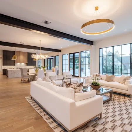 Spacious modern open-concept living area with white sofas, glass coffee table, large windows, and hardwood floors.
