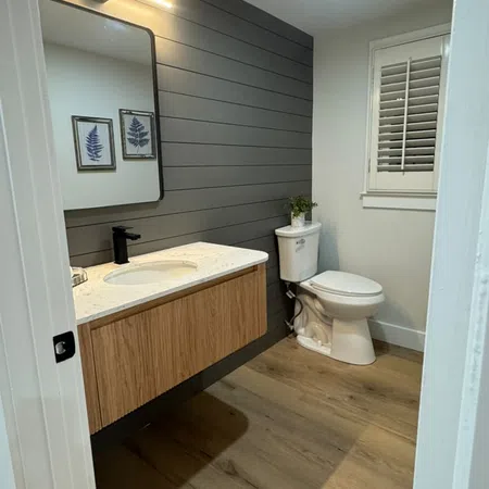 Modern bathroom with wood floating vanity, white toilet, gray shiplap wall, and botanical wall art.
