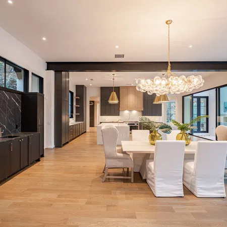 Spacious modern dining and kitchen area with wooden floors, large windows, and elegant lighting fixtures.