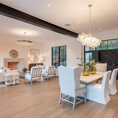 Modern open-concept living and dining room with white furniture, hardwood floors, and stylish lighting fixtures.