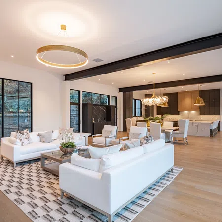 Spacious modern living room with white sofas, large windows, wooden flooring, and an open kitchen with dining area.