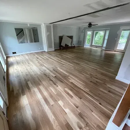Spacious empty living room with newly installed light hardwood floors and large windows letting in natural light