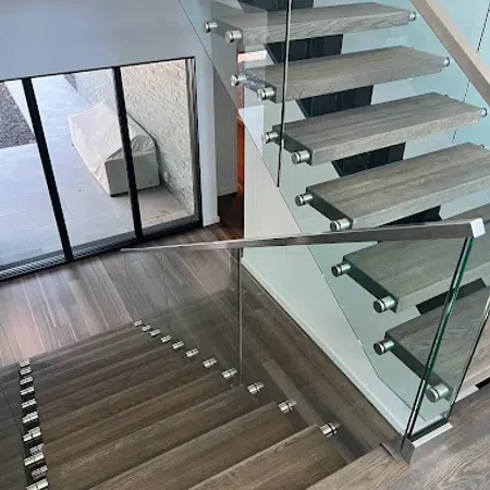 Modern floating wooden staircase with glass railing in a contemporary home interior near large windows.