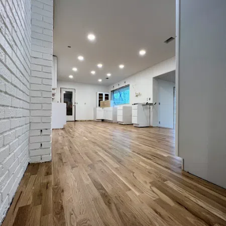 Spacious modern kitchen under construction with light wood flooring, white cabinets, and recessed ceiling lights.