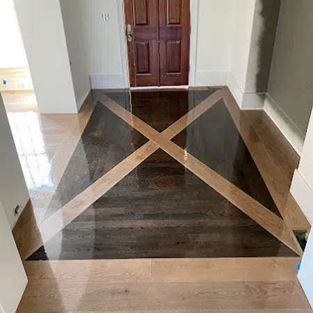 Polished hardwood floor with a geometric X pattern in front of wooden double doors in a hallway.