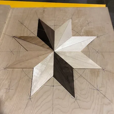 Wooden star-shaped inlay with eight pointed segments in different wood tones on a plywood base with markings.