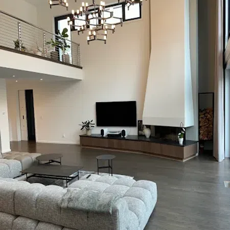 Modern living room with plush gray sectional sofa, wall-mounted TV, unique chandeliers, and tall fireplace with wood storage.