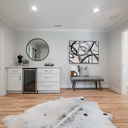 Modern entryway with white cabinets, black mini fridge, abstract art, gray bench, and cowhide rug on wood floor.