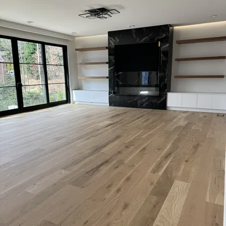 Spacious modern living room with light wood flooring, black marble fireplace, white cabinets, and large glass doors.