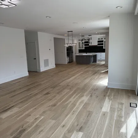 Spacious modern open-concept room with light hardwood floors, white walls, and a kitchen featuring gray cabinets and black backsplash.