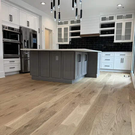 Modern kitchen with gray island, white cabinets, black subway tile backsplash, wood flooring, and pendant lights.