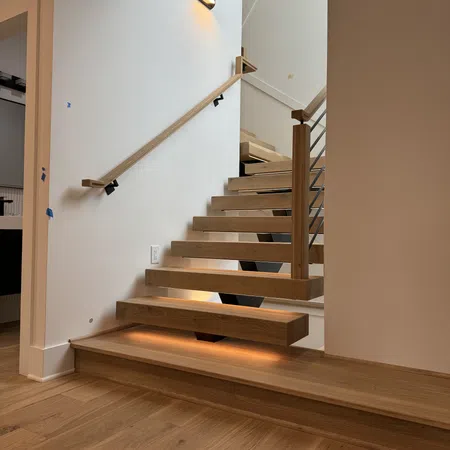 Modern floating wooden staircase with under-step lighting and a minimalist handrail in a bright interior.