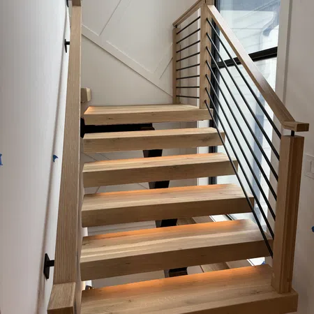 Modern wooden stairs with black metal railing and warm under-step lighting in a bright interior space