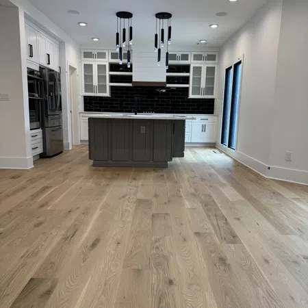 Modern kitchen with white cabinets, black backsplash, gray island, hardwood floors, and pendant lighting.