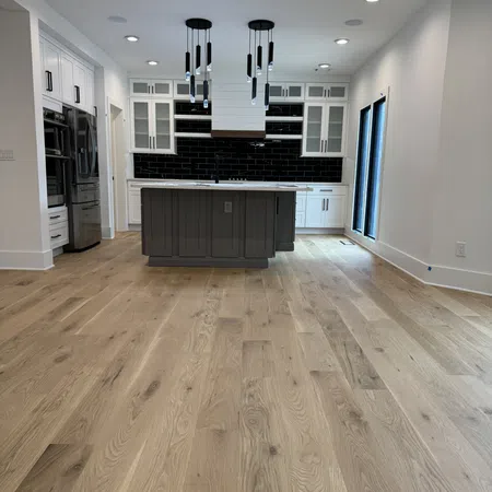 Modern kitchen with white cabinetry, black subway tile backsplash, gray island, and light wood flooring under bright lighting.