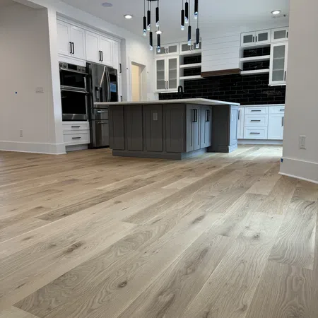 Modern kitchen with light wood flooring, gray island, white cabinets, stainless steel appliances, and black tile backsplash.