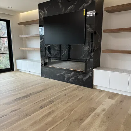 Modern living room with black marble fireplace, mounted TV, wooden shelves, and light hardwood floors